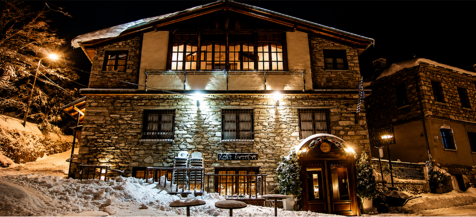 Enterne guesthouse at dusk, stone and timber facade lit warmly against the Nymfaio mountainside